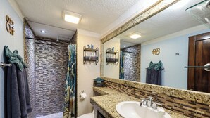 A bathroom with a granite countertop sink, a large mirror, and a shower with a mosaic tile wall.
