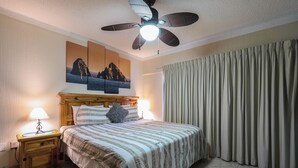 A bedroom with a bed, two bedside tables with lamps, a ceiling fan, and a large window with curtains.