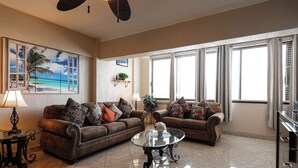 A living room with two brown leather sofas, a glass coffee table, and a ceiling fan.