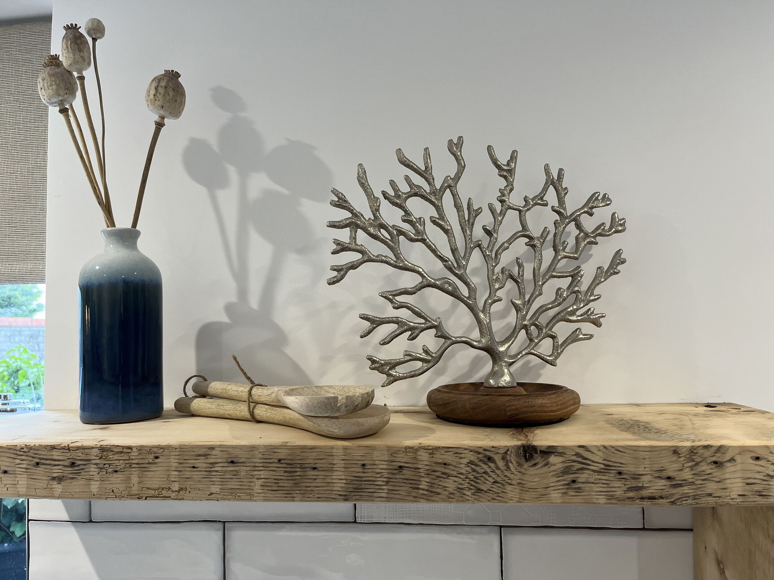 Une étagère en bois ornée d’un vase bleu, de capsules de pavot séchées, d’un bol en bois et d’une sculpture d’arbre en métal.