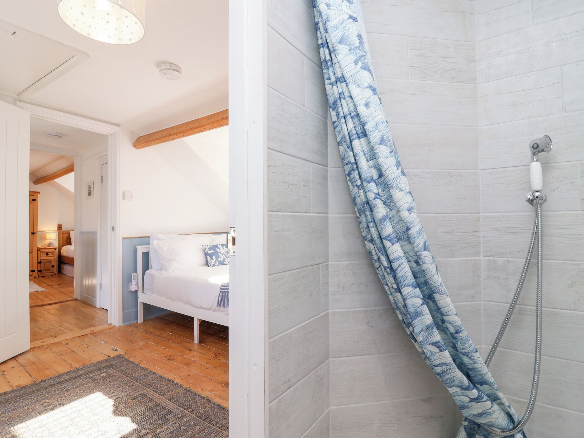 Une chambre à coucher avec un lit, une table de chevet et une commode. La salle de bain est équipée d’un rideau de douche et d’un pommeau de douche.