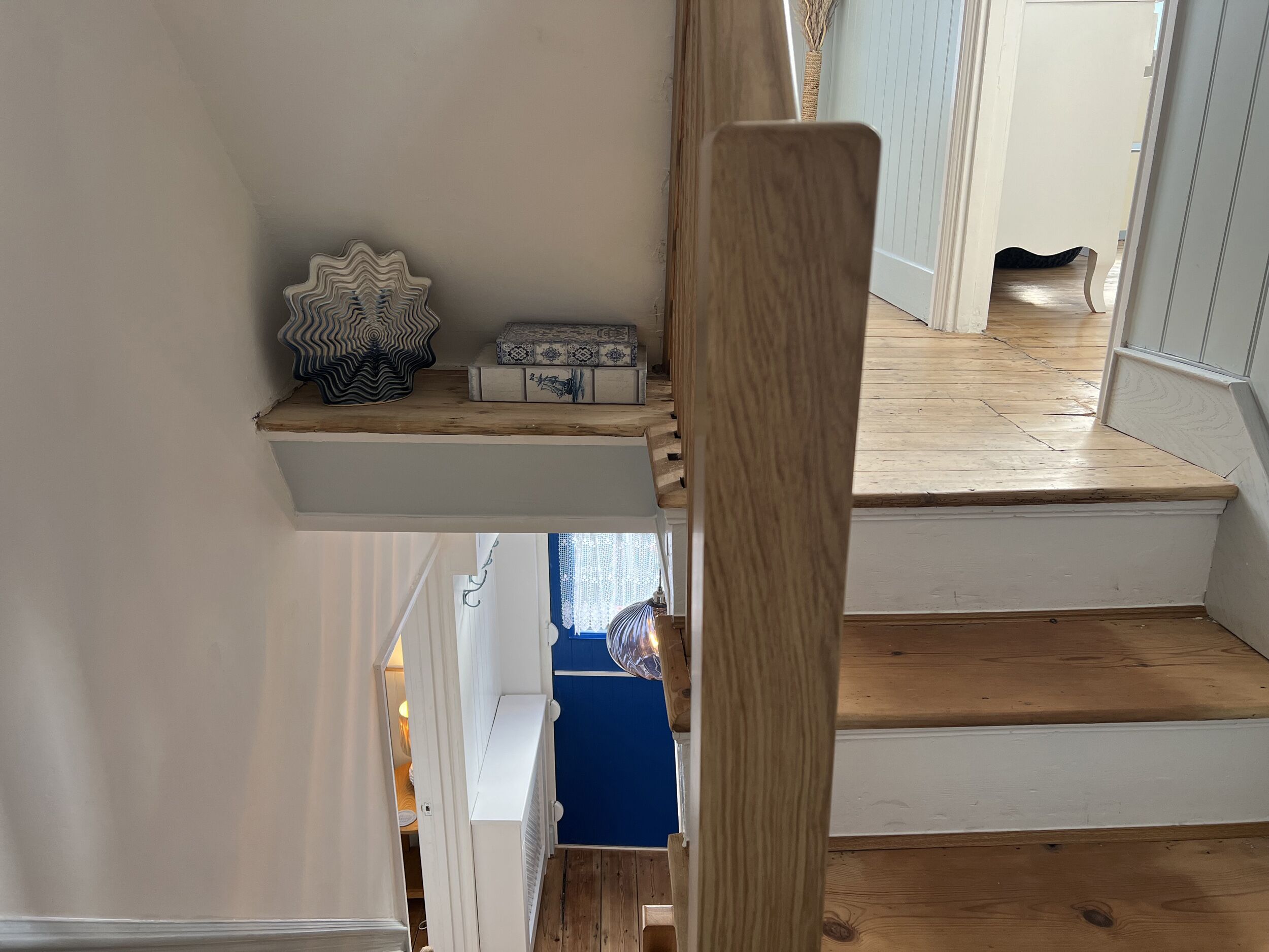 A wooden staircase with a white railing, leading to a landing with a blue wall and a white door.