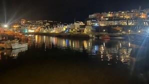 Un puerto nocturno con barcos amarrados, edificios iluminados y un árbol de Navidad en la orilla.
