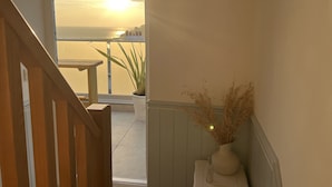 Un balcón con vista al atardecer sobre el mar, una mesa pequeña y una planta en maceta.