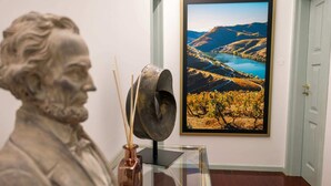 Eine Statue, ein Glastisch und ein gerahmtes Landschaftsbild in einem Raum mit weißer Tür und Holzboden.
