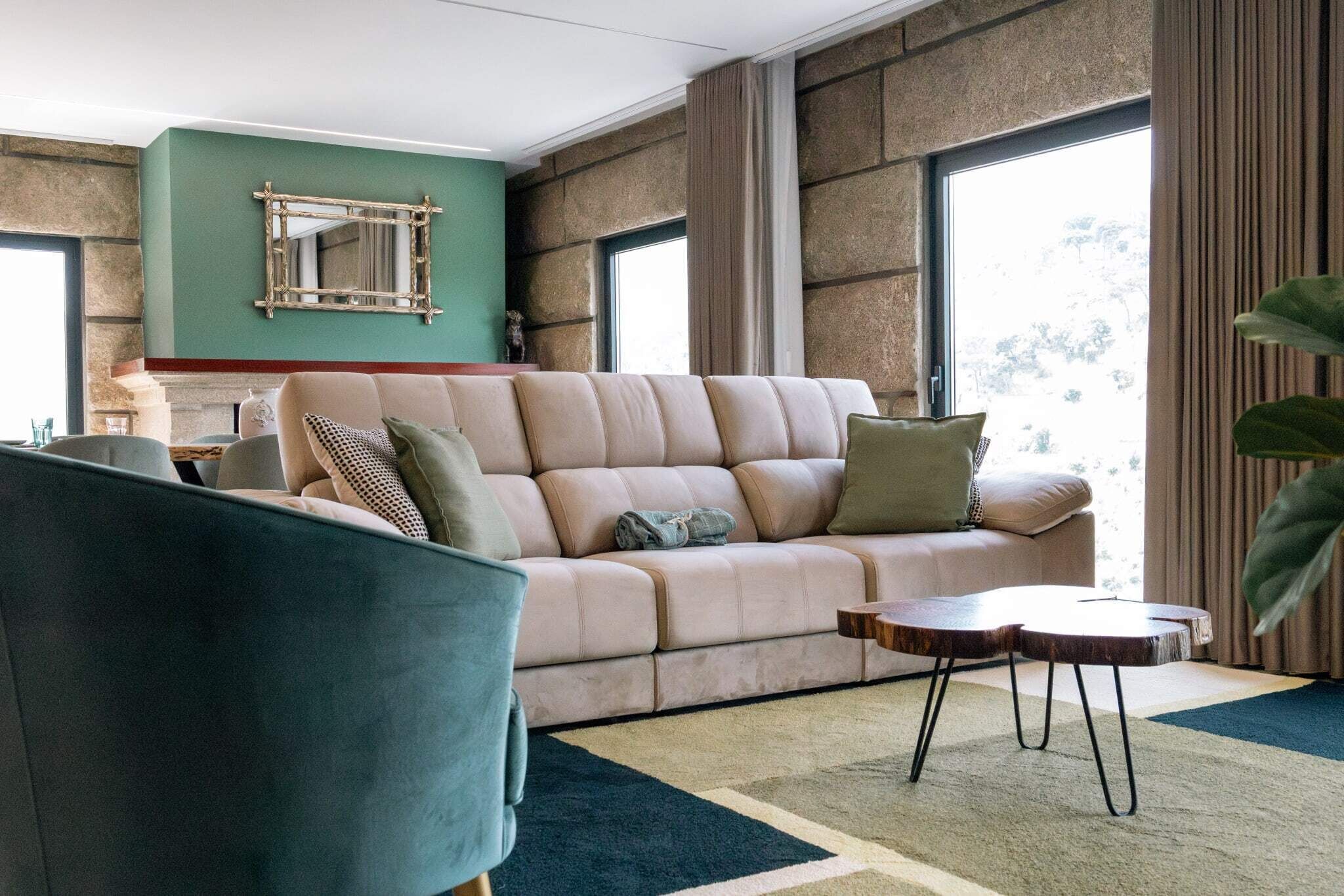 A living room with a beige sofa, a blue armchair, a wooden coffee table, and a large mirror on the wall.