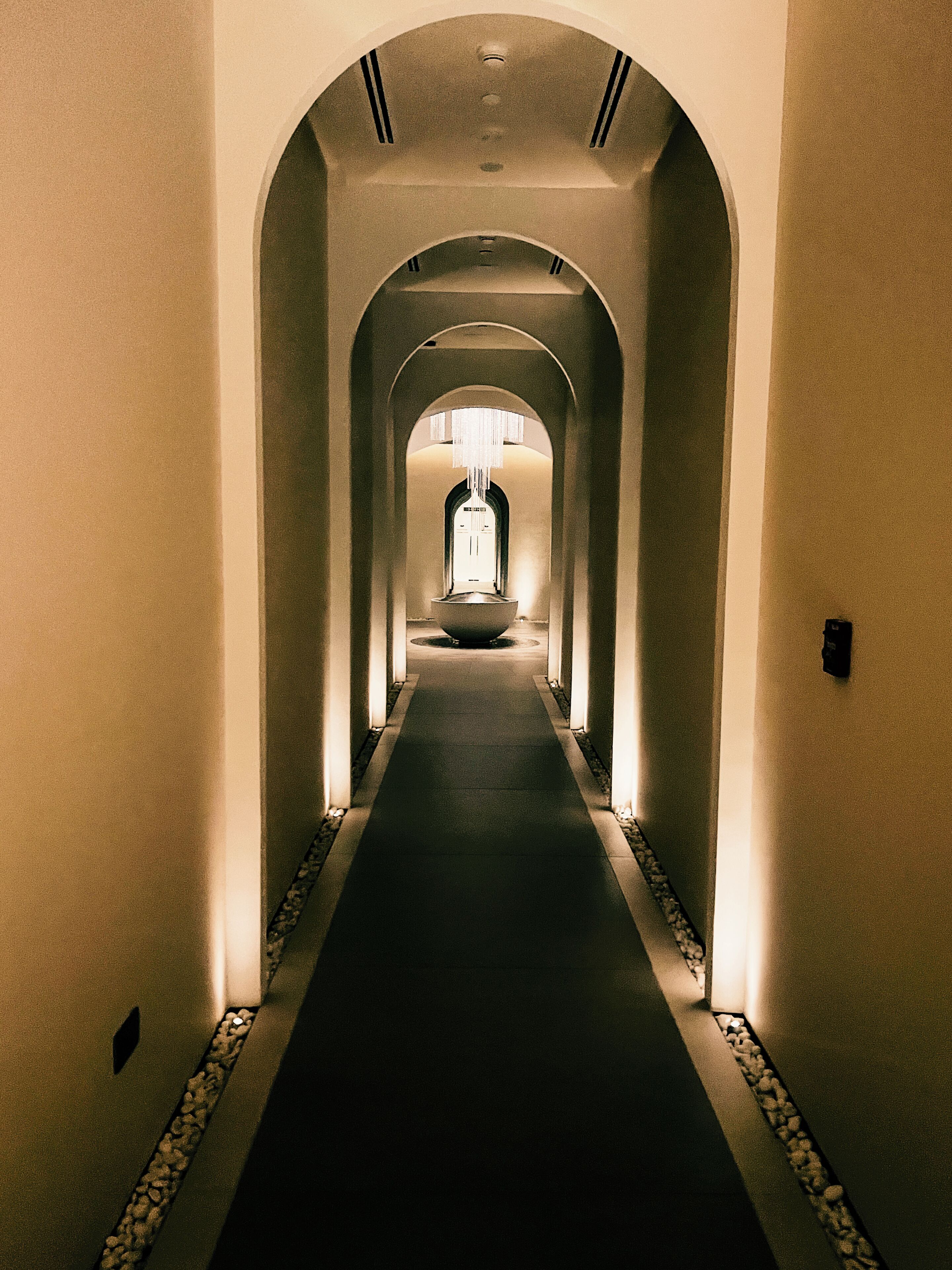 Un corridoio con archi, un lampadario al centro e un pavimento piastrellato.