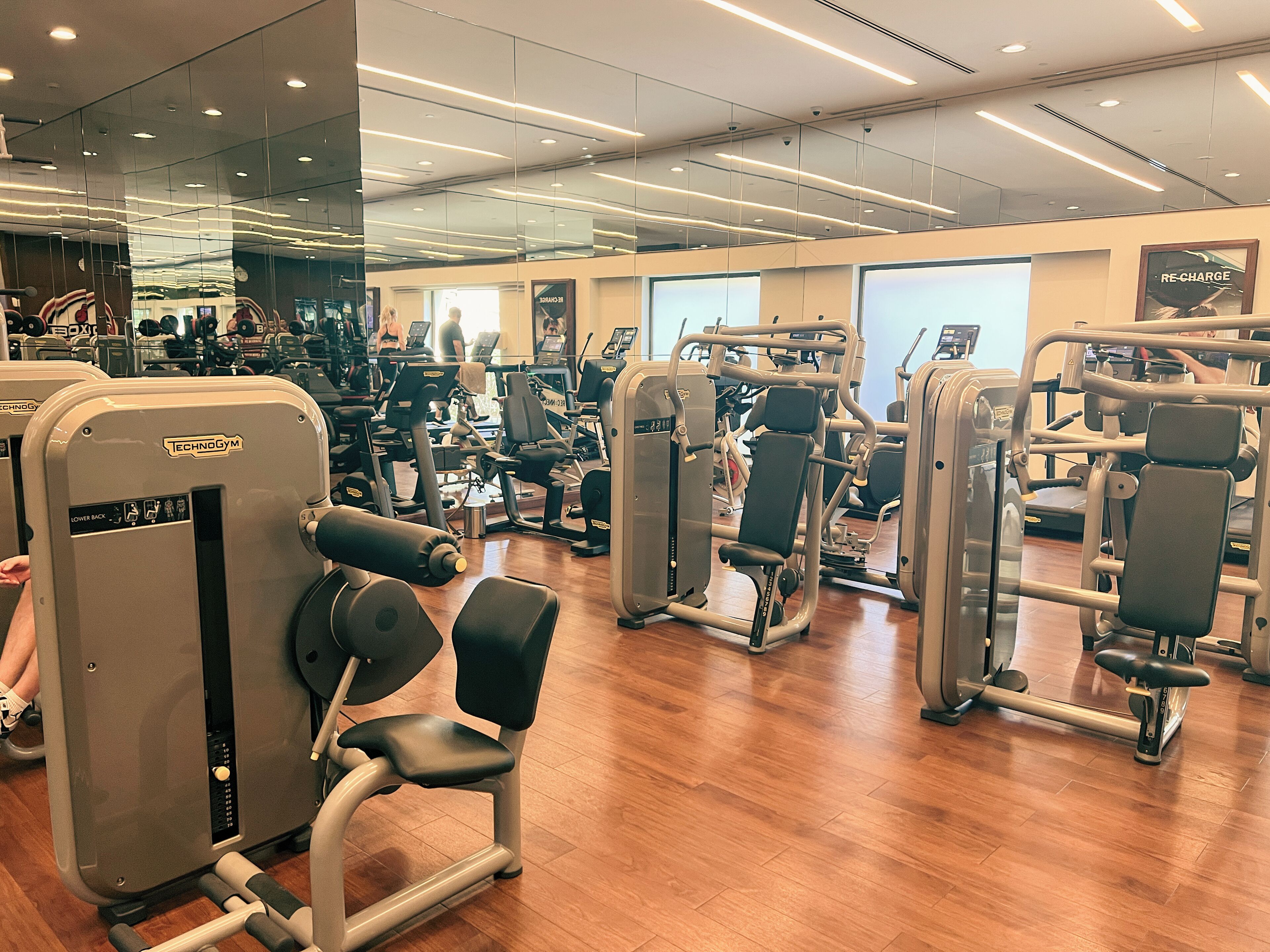 Ein Fitnessstudio mit verschiedenen Trainingsgeräten, Holzböden und großen Fenstern.