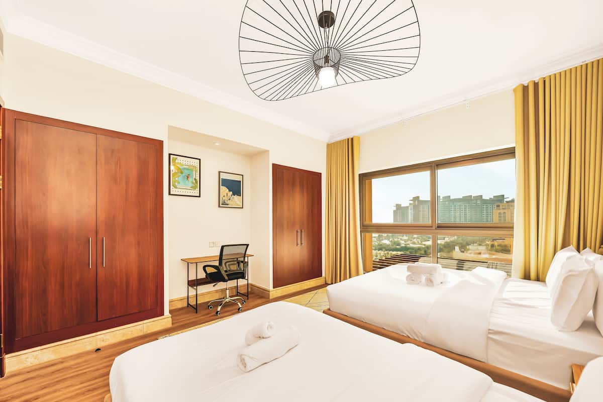 Een hotelkamer met twee bedden, een bureau en een groot raam met uitzicht op de stad.