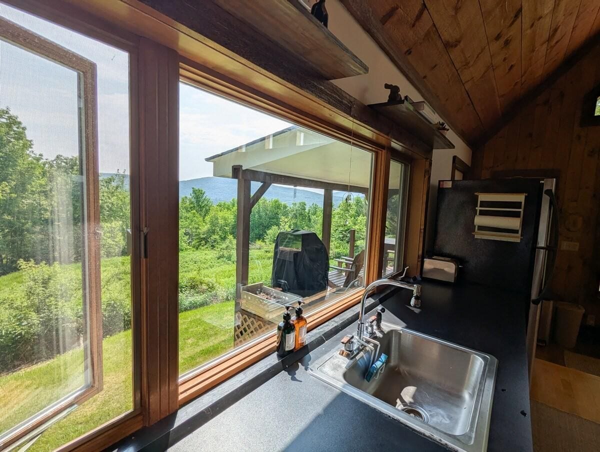 Eine Küche mit einem großen Fenster, einem Spülbecken und einem Grill draußen.