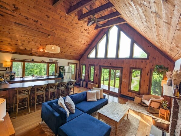 A spacious living area with a high ceiling and large windows, a kitchen with a bar, and a cozy seating area.