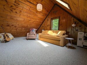 A cozy attic room with a wooden ceiling, a sofa, a chair, a guitar, and a small table. - Cozy Catskills A-frame hideaway (Margaretville)