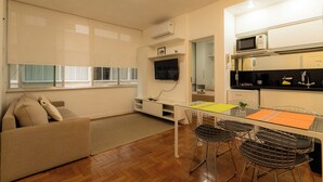 Un espacio habitable compacto con sofá, una mesa de comedor con sillas, una zona de cocina con electrodomésticos modernos y un ventanal que proporciona luz natural.