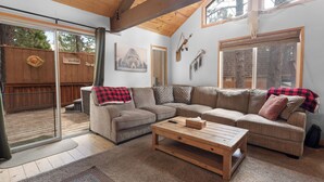 A cozy living room with a sectional sofa, a wooden coffee table, and a sliding glass door leading to a backyard. - G&P Moonridge (Big Bear Lake)