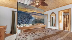 A bedroom with a large bed, a wooden desk, a television mounted on the wall, and a ceiling fan. - G&P Moonridge (Big Bear Lake)
