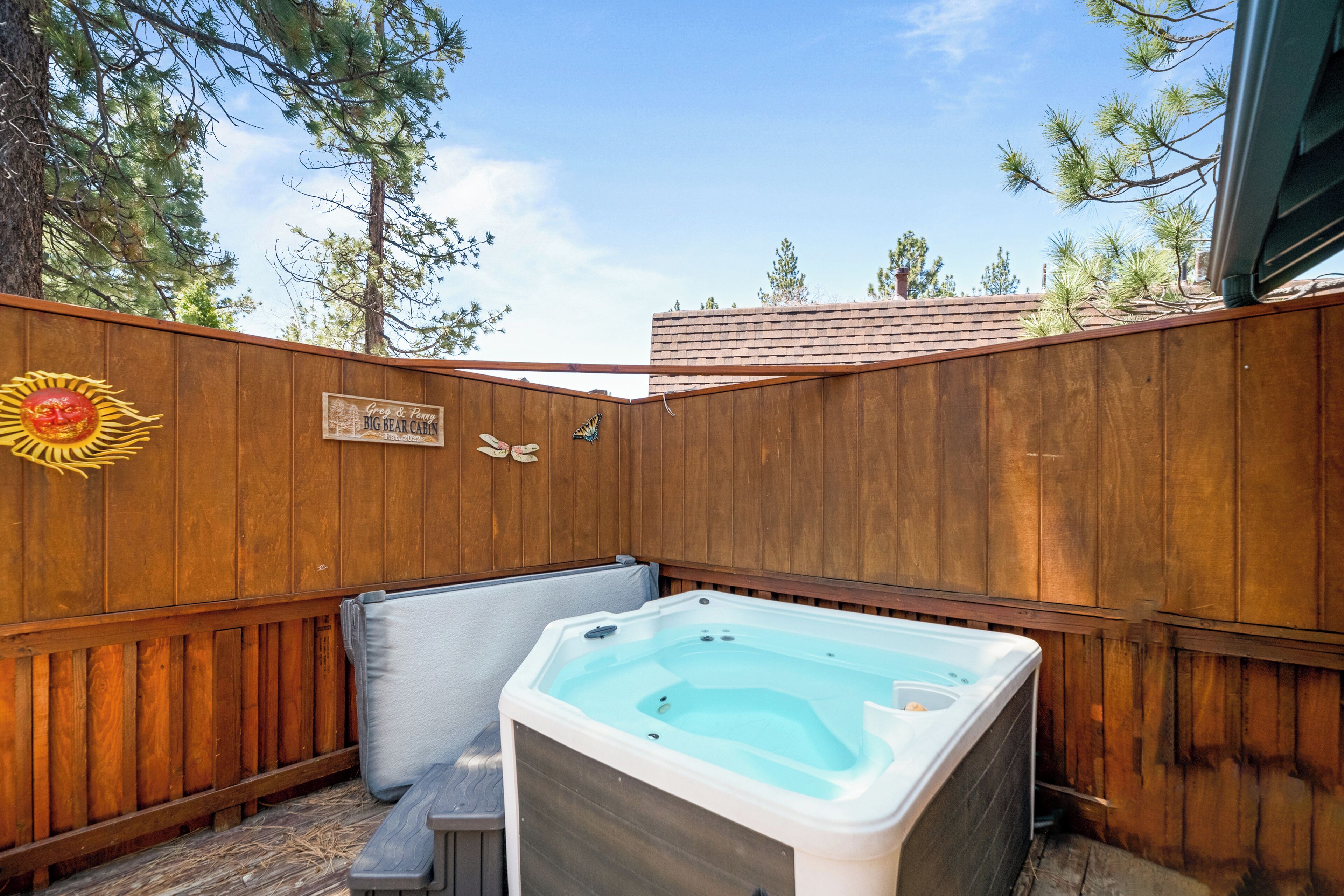 Une clôture en bois, un jacuzzi et une pancarte indiquant « Big Bear Cabin ».