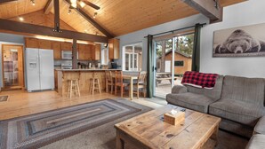 A spacious living area with a wooden ceiling, a large sofa, a coffee table, and a kitchen area with wooden cabinets and a refrigerator. - G&P Moonridge (Big Bear Lake)