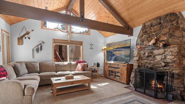A cozy living room with a stone fireplace, wooden beams, a sofa, and a television. - G&P Moonridge (Big Bear Lake)
