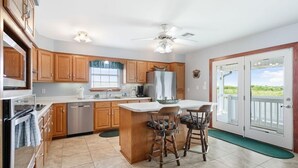 A kitchen with wooden cabinets, a central island with bar stools, a refrigerator, and a ceiling fan. - Bayou Manor: 3BR House (Slidell)
