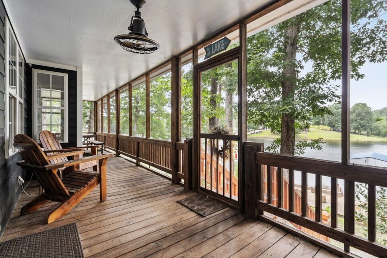 A wooden deck with a view of a lake, a sign reading 'LAKE', and a ceiling fan.