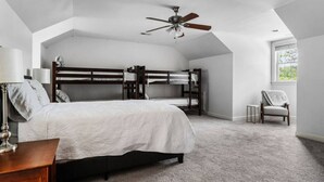 A bedroom with a bunk bed, a single bed, a ceiling fan, a chair, and a window.
