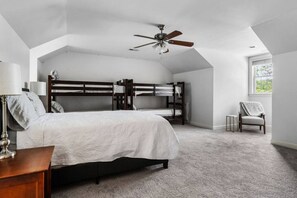 A bedroom with a bunk bed, a single bed, a ceiling fan, a chair, and a window.