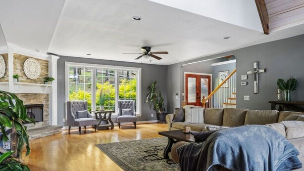 A spacious living room with a fireplace, large windows, and a staircase.