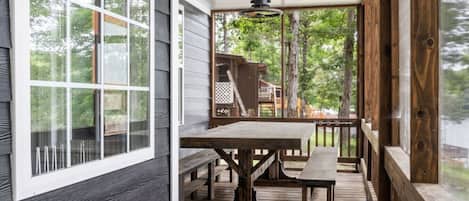 Une terrasse en bois avec une table et des bancs, donnant sur une autre terrasse dotée d’une rambarde et bordée d’arbres.