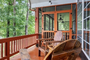 A wooden deck with a bench and chairs, large windows, and a view of the forest. - Smith Lake Serenity (Jasper)