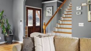 A living room with a staircase, a potted plant, and a door with frosted glass panels.