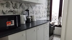 Uma cozinha com armários brancos, bancada preta, liquidificador, chaleira e janela com cortinas.