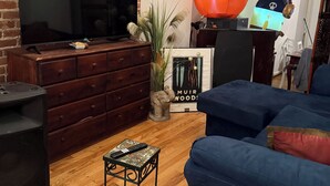 Ein Wohnzimmer mit Backsteinwand, Flachbildfernseher, blauem Sofa, kleinem Tisch mit Fernbedienung und Halloween-Dekorationen.