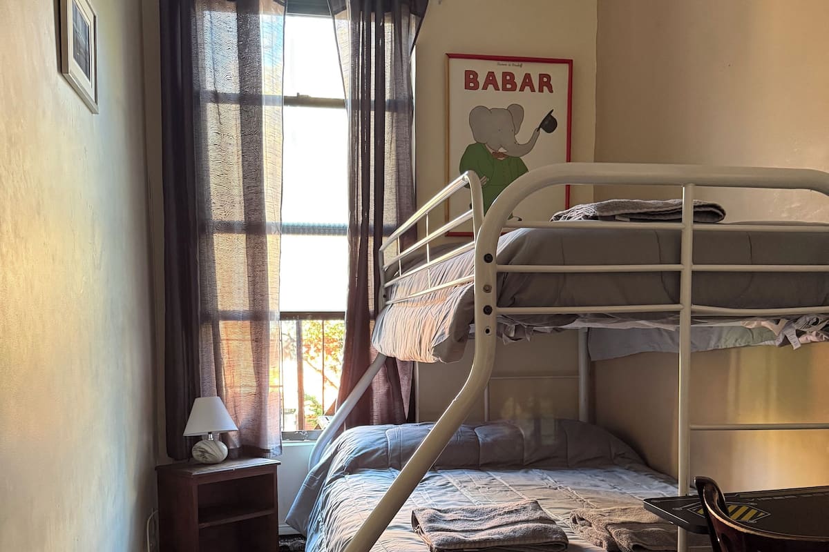 A bunk bed room with a window, a lamp, a poster, and a chair.