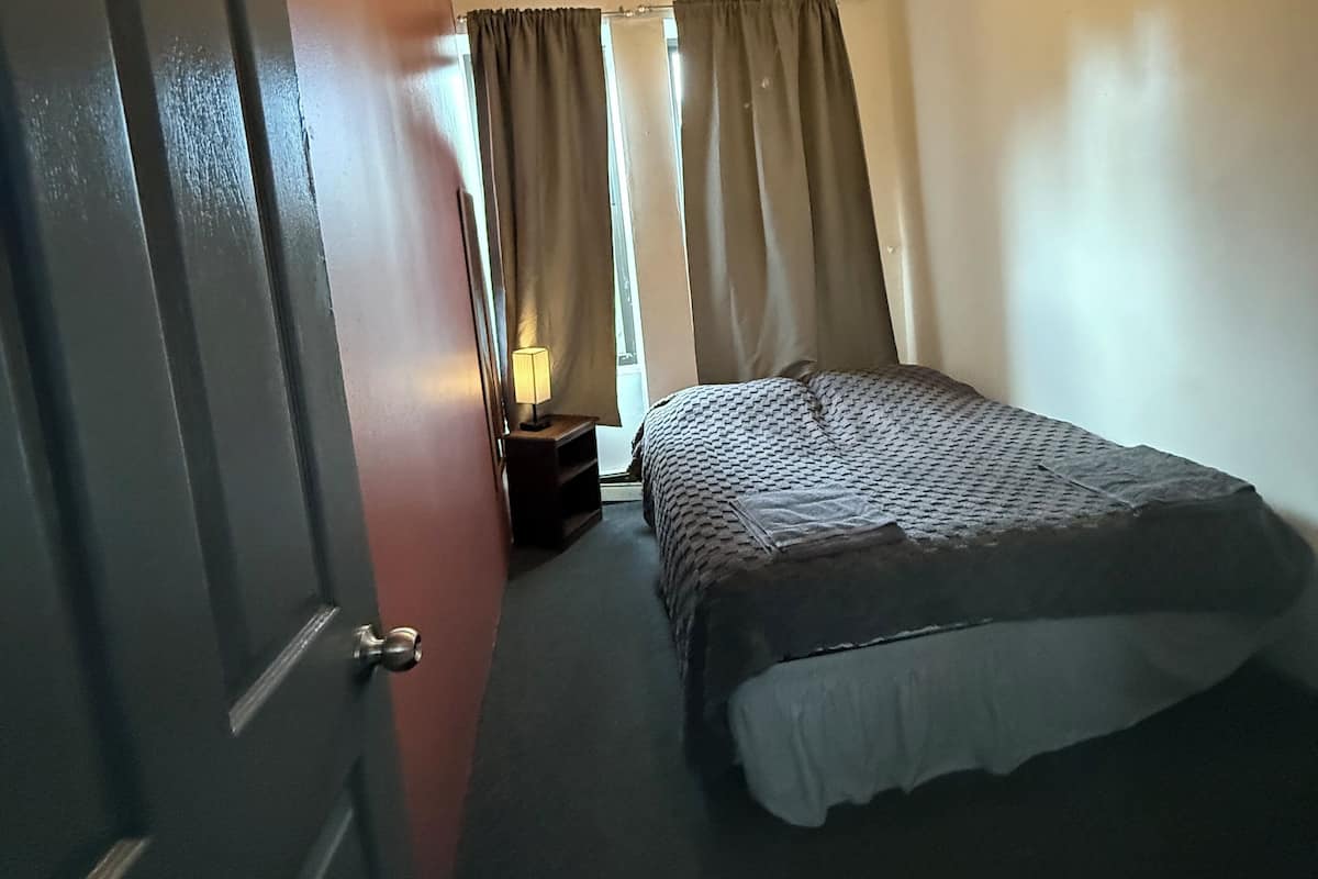 A hotel room with a bed, a ceiling fan, a nightstand with a lamp, and a door.