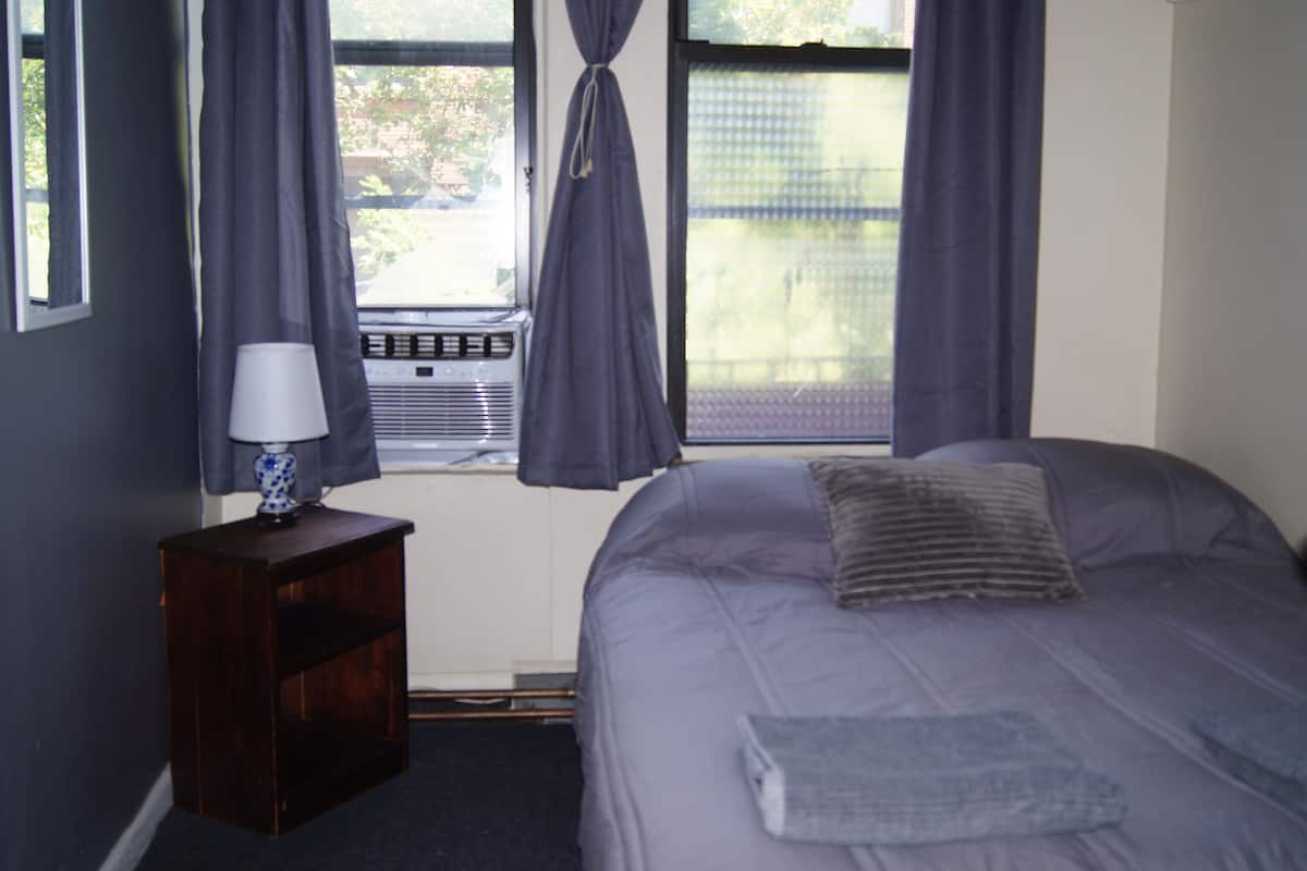 A bedroom with a bed, a nightstand, a lamp, and a window with curtains.