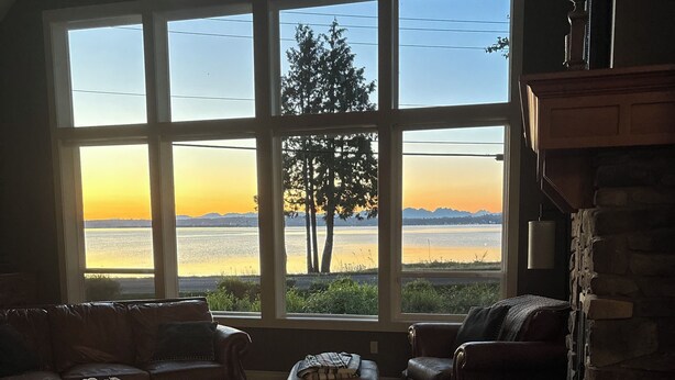 Ein gemütliches Wohnzimmer mit großem Fenster mit Blick auf ein Gewässer und Bäume, ausgestattet mit Ledersofas und einem Holztisch.