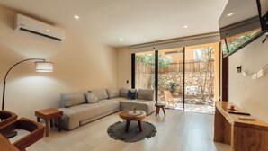 A modern living room with a sofa, coffee table, and a lamp. There is a sliding glass door leading to an outdoor area with a bamboo fence and stone wall. - Aldea Savia hideaway in Tulum (Tulum)