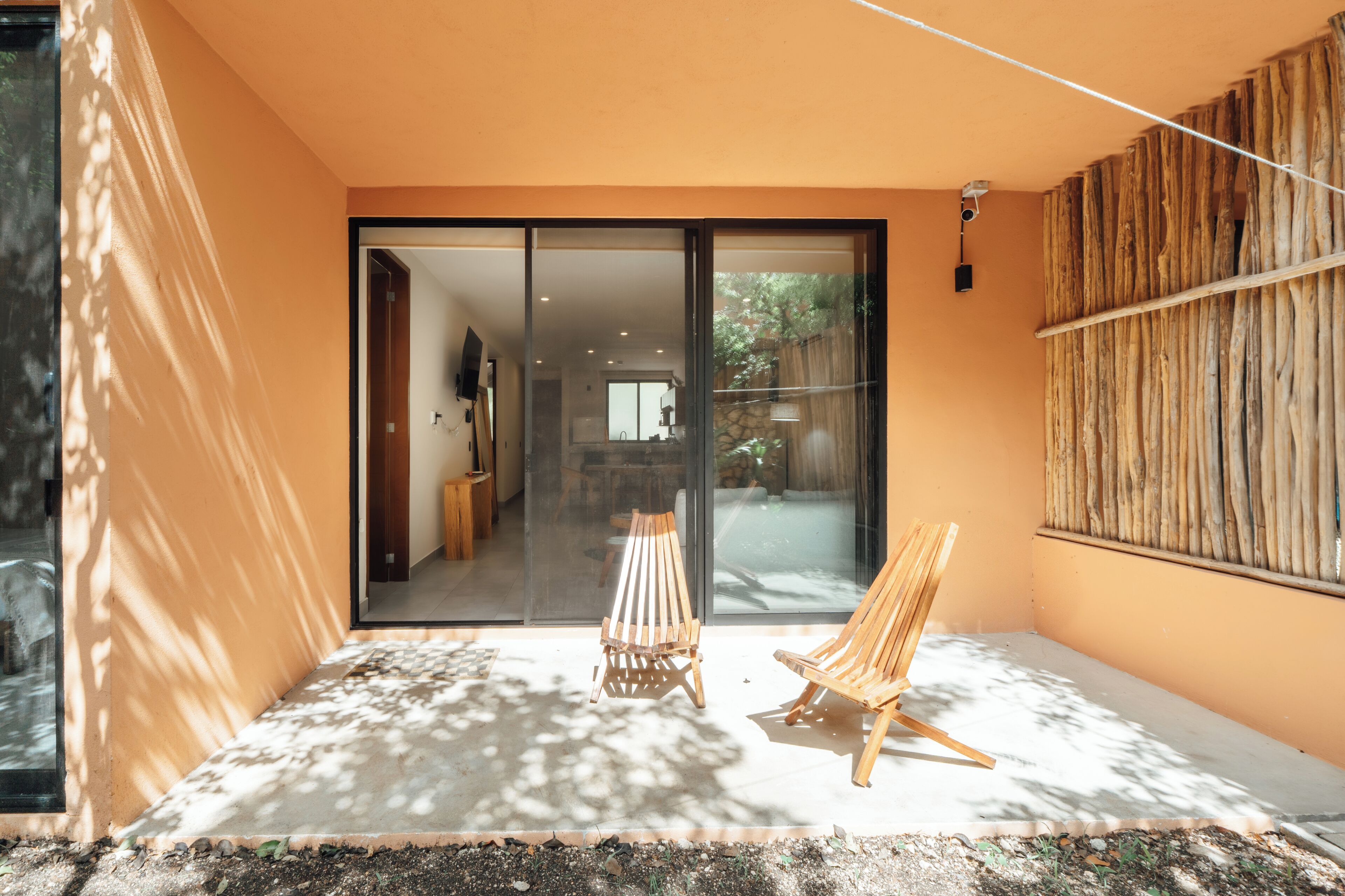 Un intérieur moderne avec une porte-fenêtre coulissante donnant sur un coin repas. Deux chaises en bois sont placées à l’extérieur de la porte.