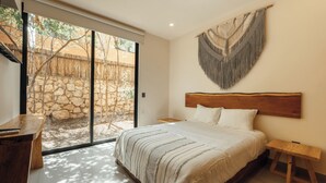 A bedroom with a large bed, a wooden headboard, a stone wall, and a view of a courtyard. - Aldea Savia hideaway in Tulum (Tulum)