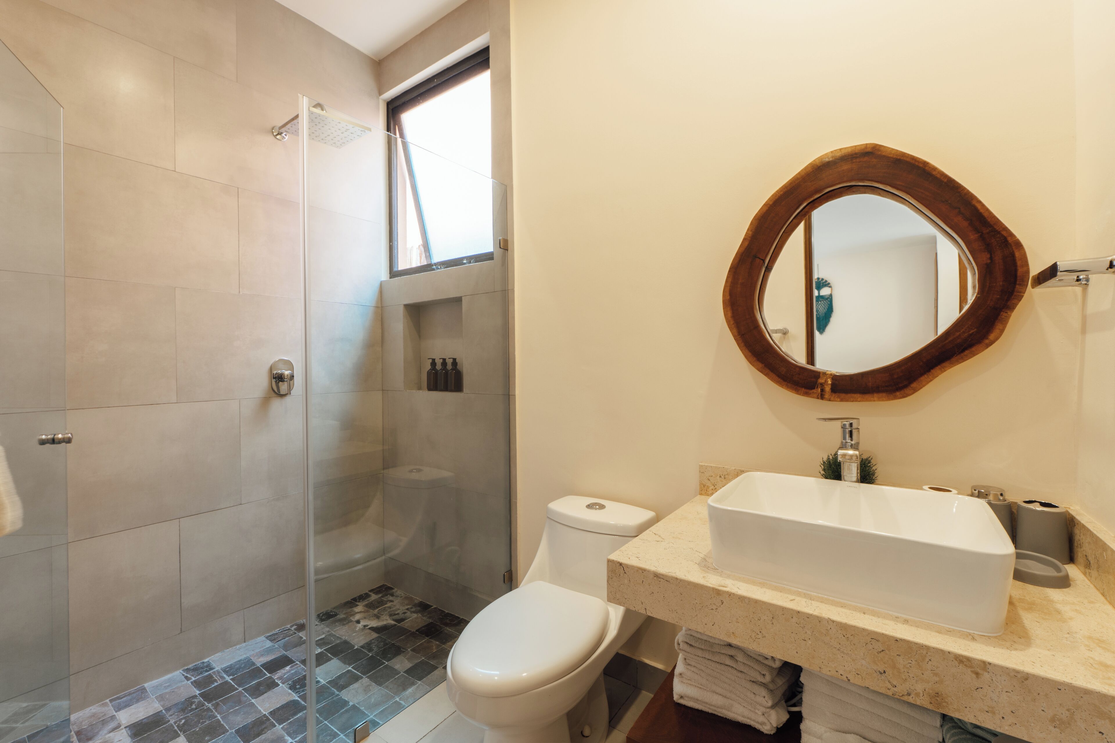 A bathroom with a glass-enclosed shower, a toilet, and a sink with a mirror above it.