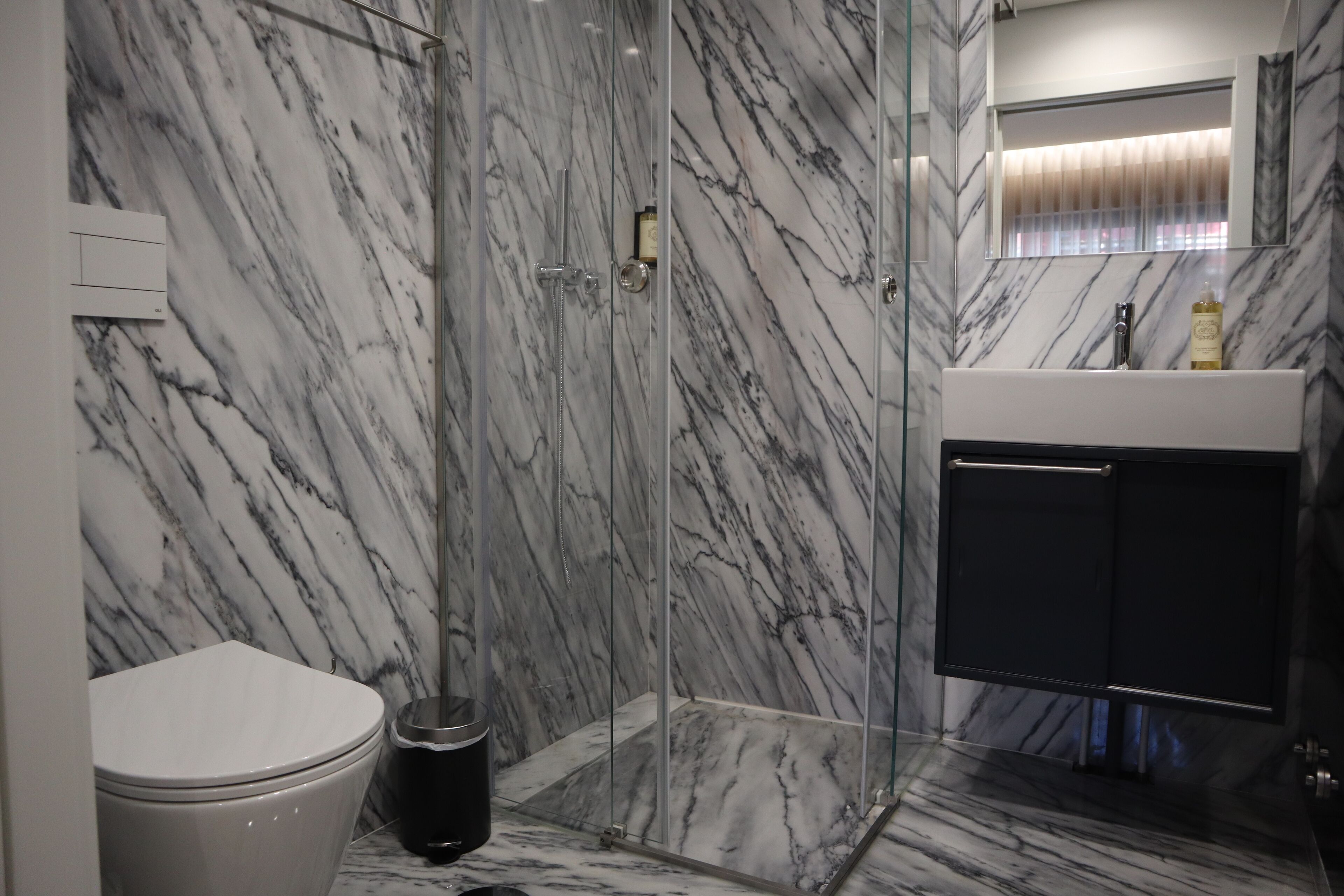 A bathroom with a glass-enclosed shower, a white toilet, and a marble backsplash.