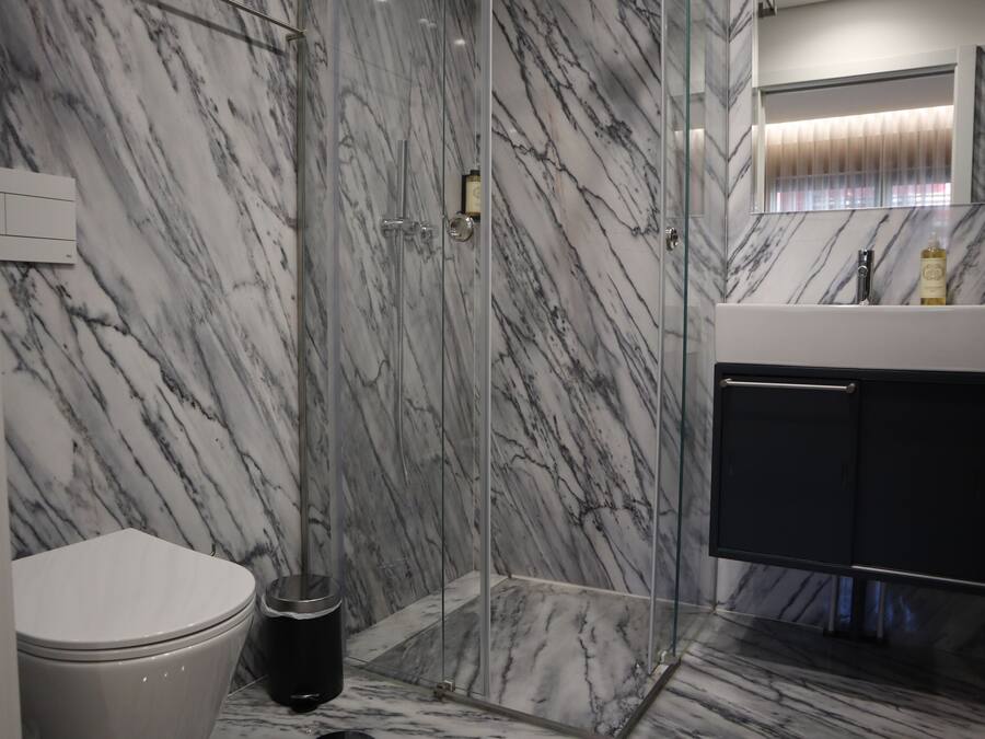 A bathroom with a glass-enclosed shower, a white toilet, and a marble backsplash.