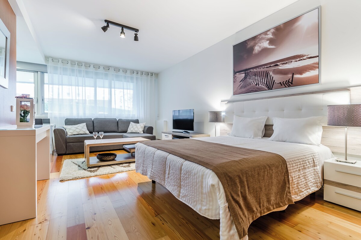 Ein modernes Hotelzimmer mit einem großen Bett, einer Couch, einem Fernseher und einem Gemälde an der Wand.