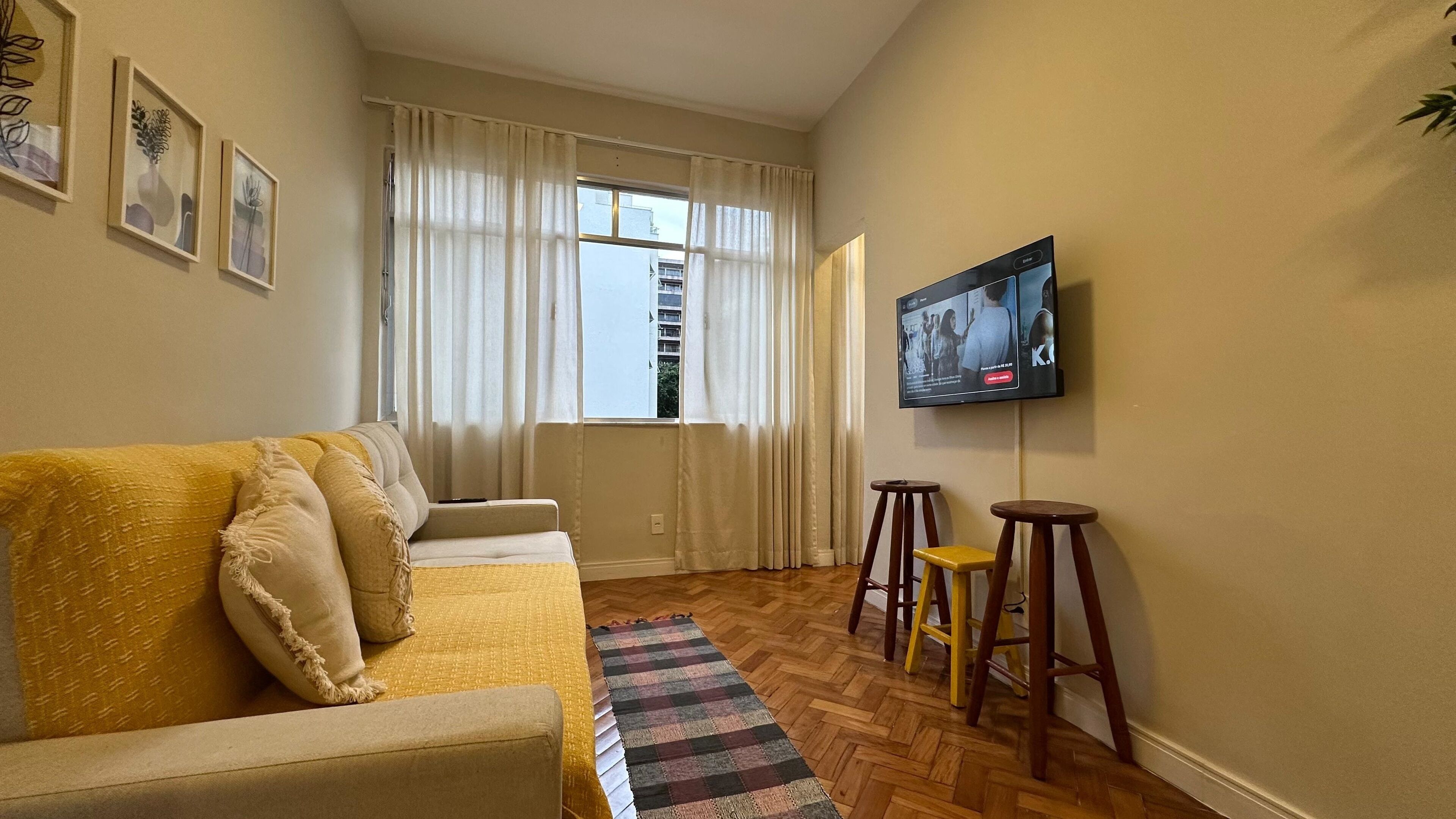 A living room with a sofa, a television mounted on the wall, and a window with curtains.