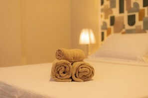 A neatly made bed with rolled towels and a lamp in the background. - SUH Copacabana 111 Plus Apartment (Rio de Janeiro)