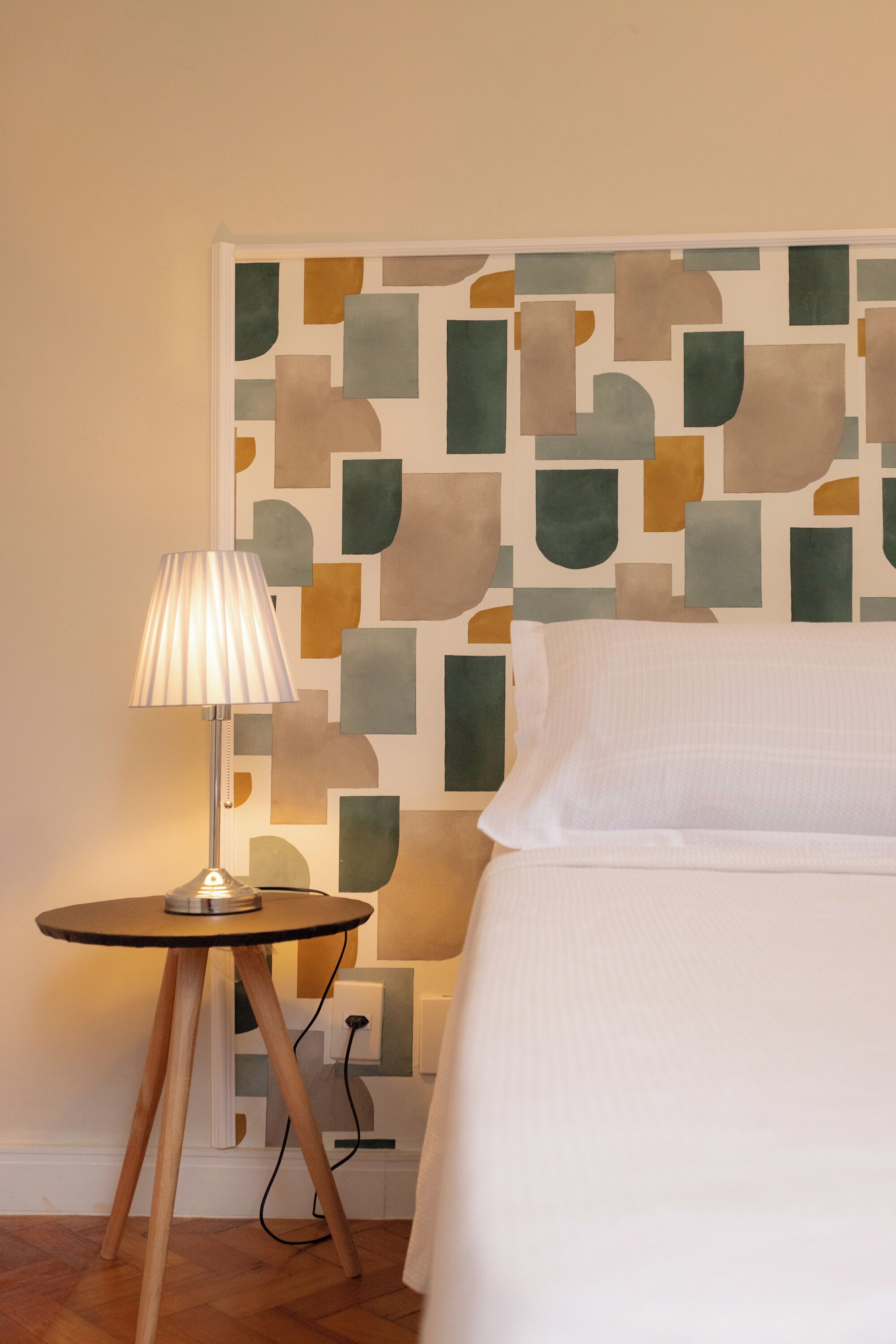 A neatly made bed with a white pillow and a lamp on a small wooden table beside it.