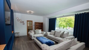 A modern living room with two white sofas, a blue throw blanket, and a wooden bookshelf.
