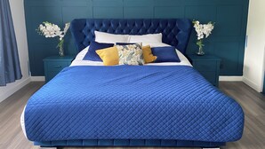 A bedroom with a large bed, teal walls, and two nightstands with vases of flowers.