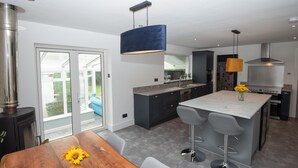 A modern kitchen with a central island, bar stools, and a dining table with a vase of sunflowers.