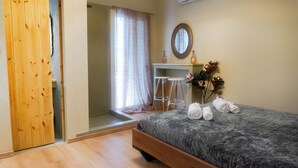 Een slaapkamer met een bed, een houten garderobe, een badkamer met douche en een klein bureau met krukjes.